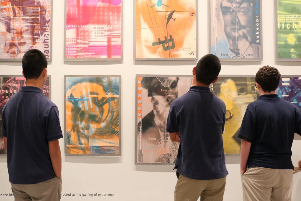 photograph of three youths in navy blue polo shirts looking at posters on a wall
