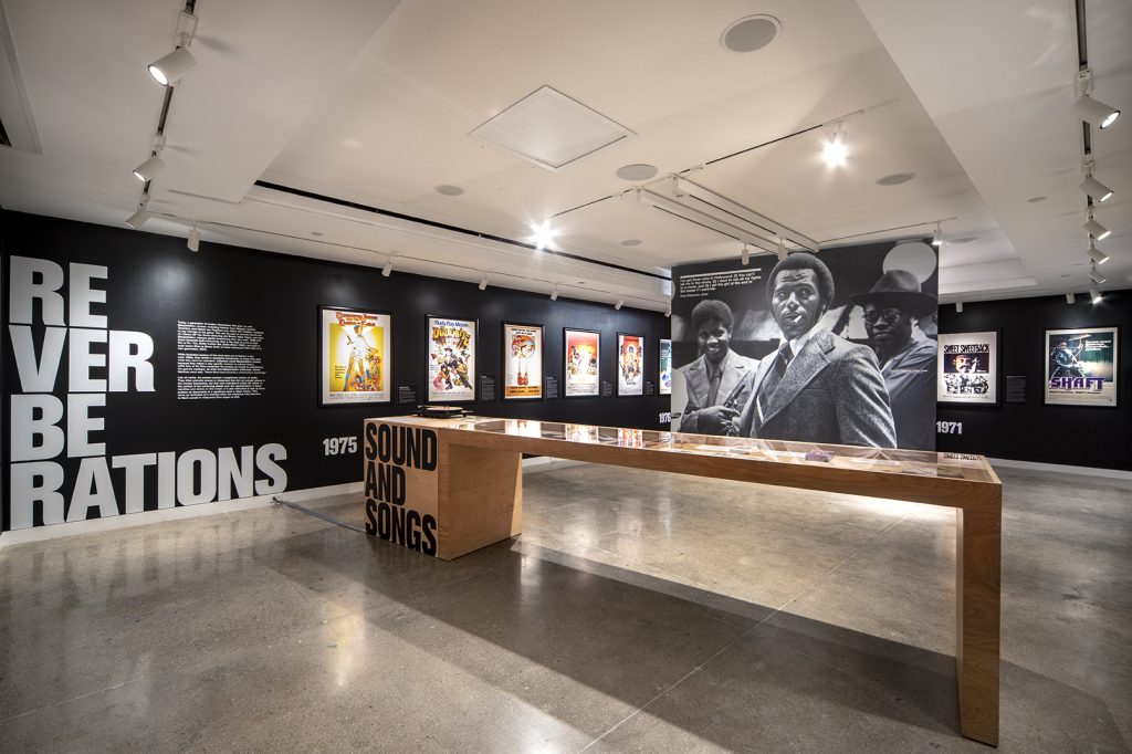 A gallery space with a long display case and a poster of a Black man in a suit.